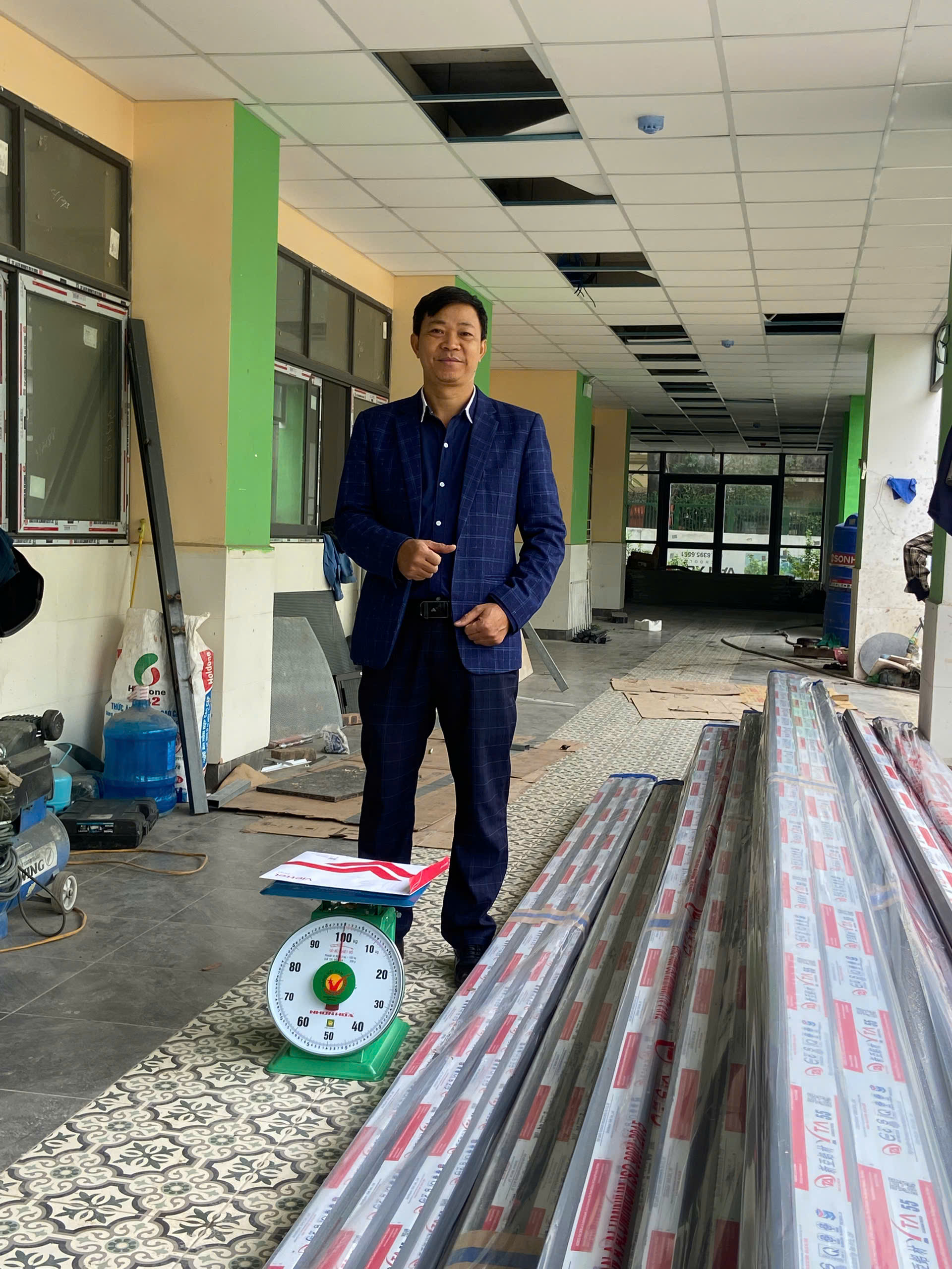 Người đàn ông đứng cạnh các bó thanh nhôm kính và cân đồng hồ trong công trình đang thi công